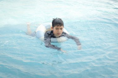 Yüzme yüzüklü mutlu Asyalı çocuk mavi suda yüzüyor. Yaz tatilinde açık havuzda şişme yüzükle oynayan rahatlatıcı çocuk. Hafta sonu havuzda yüzen neşeli çocuk.
