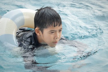 Yüzme yüzüklü mutlu Asyalı çocuk mavi suda yüzüyor. Yaz tatilinde açık havuzda şişme yüzükle oynayan rahatlatıcı çocuk. Hafta sonu havuzda yüzen neşeli çocuk.