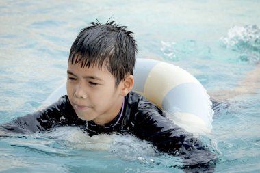 Yüzme yüzüklü mutlu Asyalı çocuk mavi suda yüzüyor. Yaz tatilinde açık havuzda şişme yüzükle oynayan rahatlatıcı çocuk. Hafta sonu havuzda yüzen neşeli çocuk.