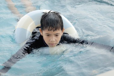 Yüzme yüzüklü mutlu Asyalı çocuk mavi suda yüzüyor. Yaz tatilinde açık havuzda şişme yüzükle oynayan rahatlatıcı çocuk. Hafta sonu havuzda yüzen neşeli çocuk.