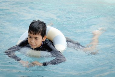 Yüzme yüzüklü mutlu Asyalı çocuk mavi suda yüzüyor. Yaz tatilinde açık havuzda şişme yüzükle oynayan rahatlatıcı çocuk. Hafta sonu havuzda yüzen neşeli çocuk.