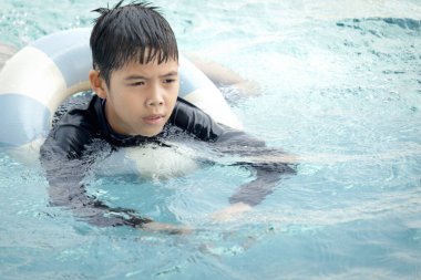 Yüzme yüzüklü mutlu Asyalı çocuk mavi suda yüzüyor. Yaz tatilinde açık havuzda şişme yüzükle oynayan rahatlatıcı çocuk. Hafta sonu havuzda yüzen neşeli çocuk.