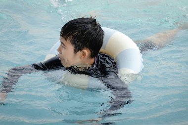 Yüzme yüzüklü mutlu Asyalı çocuk mavi suda yüzüyor. Yaz tatilinde açık havuzda şişme yüzükle oynayan rahatlatıcı çocuk. Hafta sonu havuzda yüzen neşeli çocuk.