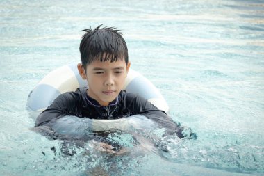 Yüzme yüzüklü mutlu Asyalı çocuk mavi suda yüzüyor. Yaz tatilinde açık havuzda şişme yüzükle oynayan rahatlatıcı çocuk. Hafta sonu havuzda yüzen neşeli çocuk.