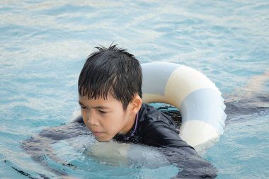 Yüzme yüzüklü mutlu Asyalı çocuk mavi suda yüzüyor. Yaz tatilinde açık havuzda şişme yüzükle oynayan rahatlatıcı çocuk. Hafta sonu havuzda yüzen neşeli çocuk.