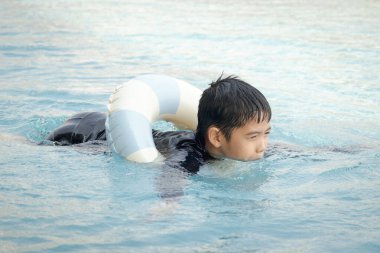 Yüzme yüzüklü mutlu Asyalı çocuk mavi suda yüzüyor. Yaz tatilinde açık havuzda şişme yüzükle oynayan rahatlatıcı çocuk. Hafta sonu havuzda yüzen neşeli çocuk.