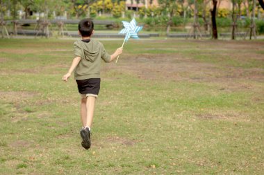Güneşli bir günde parkta rüzgar türbiniyle oynayan mutlu Asyalı çocuk. Doğada rüzgar türbini olan neşeli bir çocuk. Neşeli küçük çocuk bahçede vakit geçiriyor. Çocukluk açık hava konsepti.
