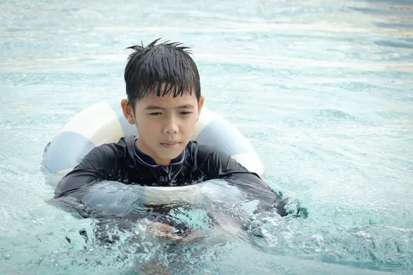 Yüzme yüzüklü mutlu Asyalı çocuk mavi suda yüzüyor. Yaz tatilinde açık havuzda şişme yüzükle oynayan rahatlatıcı çocuk. Hafta sonu havuzda yüzen neşeli çocuk.