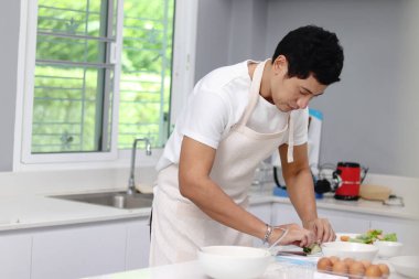 Önlüklü Asyalı adam mutfakta sağlıklı kahvaltı hazırlıyor. Mutlu adam evde yemek pişiriyor.. 