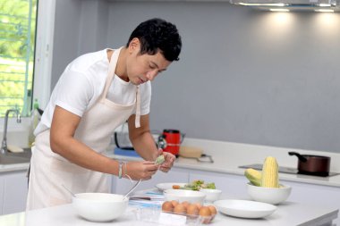 Önlüklü Asyalı adam mutfakta sağlıklı kahvaltı hazırlıyor. Mutlu adam evde yemek pişiriyor.. 