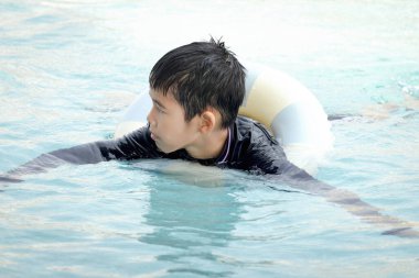 Yüzme yüzüklü mutlu Asyalı çocuk mavi suda yüzüyor. Yaz tatilinde açık havuzda şişme yüzükle oynayan rahatlatıcı çocuk. Hafta sonu havuzda yüzen neşeli çocuk.