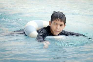 Yüzme yüzüklü mutlu Asyalı çocuk mavi suda yüzüyor. Yaz tatilinde açık havuzda şişme yüzükle oynayan rahatlatıcı çocuk. Hafta sonu havuzda yüzen neşeli çocuk.