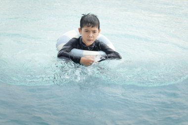 Yüzme yüzüklü mutlu Asyalı çocuk mavi suda yüzüyor. Yaz tatilinde açık havuzda şişme yüzükle oynayan rahatlatıcı çocuk. Hafta sonu havuzda yüzen neşeli çocuk.