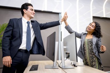 Genç iş adamları ofisteki masaüstü bilgisayarlarına beşlik çakıyor. İki iş arkadaşı beşlik çaktı. İş adamı ve iş kadını bu başarıyı kutlamak için beşlik çakıyor..