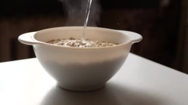 Beyaz bir tabak yulaf ezmesi kaynar suyla doldurulur. Yulaf lapası dökülürken, kurşun şeffaf bir buhar vardır..