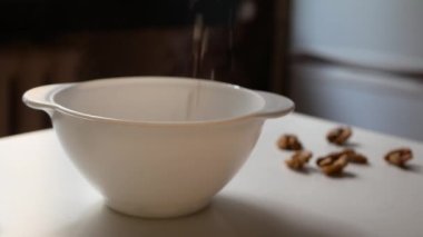 Yulaf ezmesi ve cevizden oluşan hızlı bir kahvaltı hazırlıyorum. Ön planda mısır gevreğinin döküldüğü beyaz bir tabak ve arka planda ceviz var..