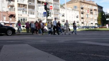 İnsanlar trafik çevirmesi sırasında geniş bir caddeden geçiyorlar. Arka planda güneşin aydınlattığı güzel tarihi evler var..