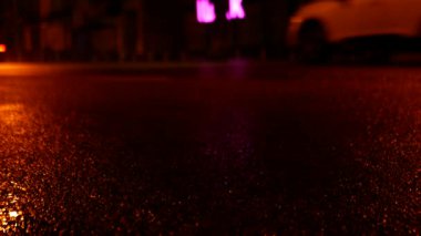 Gece şehrinde arabaların ıslak asfalt üzerinde hareketi. Asfalt seviyesinden statik atış.