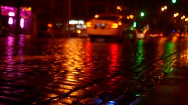 Bir polis arabası gece kaldırımlı bir yolda bir çağrı alıyor. Islak yolda, tüm renkli ışıklar yansır..
