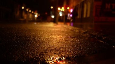 Geceleri şehrin orta kesiminde ıslak asfalt yol. Yolun sadece geçen kısmı odak noktasında, tek başına yürüyenler defocus 'ta görülebilir..