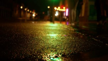 Yolu olan nemli bir gece sokağı ve yürüyen insanlarla dolu bir kaldırım. Geceleri sarı ışıkla zemin katta çekim yapmak..