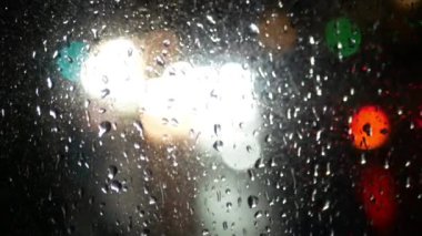 Geceleri arabaların yağmur sırasında arabanın camından geçişi. Ön planda, bir arabanın camına çöp damlaları saçılmış..