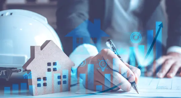 Emlak piyasası verilerini, emlak teknolojisi ve finansmanı temsil eden holografik modeller, sabit şapka ve çubuk grafikleriyle analiz eden eller.