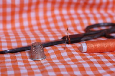 Portakal rengi ve beyaz kareli kumaş. Yüksük ve turuncu iplikli. Arkaplanda Klasik Makas