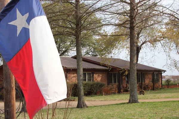 Texas Flag With Brick Ranch House in Background Shallow DOF