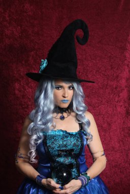 Woman Dressed as Blue Witch Holding Crystal Ball With Red Background