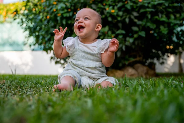 小婴儿坐在自家花园的草地上 一边张开嘴一边大声笑 一边举手 童年时代的乐趣 — 图库照片