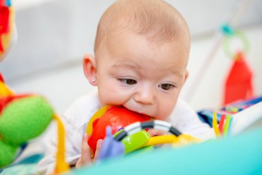 Bebek çocuk parkında yatıp oyuncağı ısırıyor. İlk dişlerin ortaya çıkmasından kaynaklanan sakız rahatsızlığını gidermek için. Yeni doğan bebeğe sağlık ve bakım kavramı
