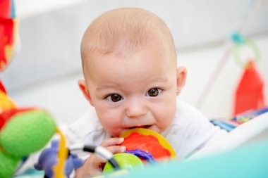 Bebek çocuk parkında yatıp oyuncağı ısırıyor. İlk dişlerin ortaya çıkmasından kaynaklanan sakız rahatsızlığını gidermek için. Yeni doğan bebeğe sağlık ve bakım kavramı
