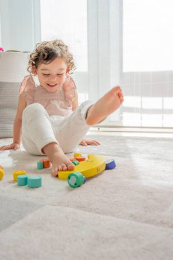 Renkli, sürdürülebilir tahta parçalarıyla oynarken gülümseyen bir kızın dikey fotoğrafı. Montessori malzemeleri. çocuklukta gelişme ve öğrenme