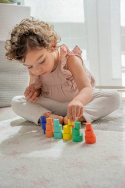 Pembe elbiseli güzel küçük bir kız konsantre bir şekilde kuleler, istifleme blokları ve renkli ahşap parçalar yapıyor. montessori maddi gelişim, çocuk oyununda yaratıcılık ve hayal gücü