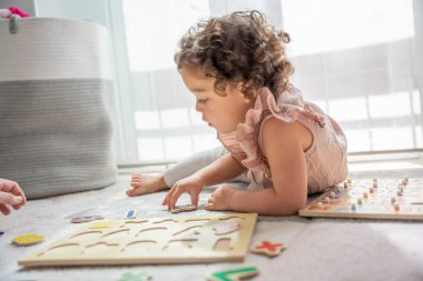 Küçük bir kızın tahta alfabe harfleriyle oynayan bir oyun hasırının üzerine uzanmış görüntüsü. Montessori metodolojisi ve malzemeleri. Çocukluk döneminde eğitim, gelişme ve öğrenme.