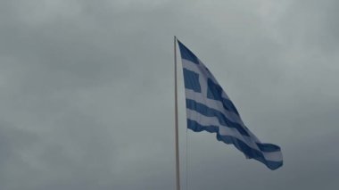 Video, bulutlu bir sonbahar gününde direkte sallanan bir Yunan bayrağını gösteriyor.