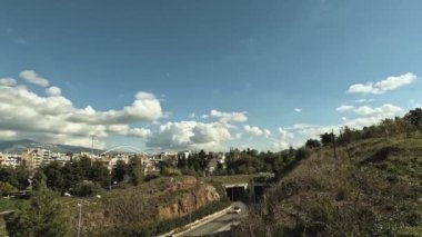 Time lapse video shot from a hill shows cars moving on a road with clouds passing by in the blue sky at suburb of Athens-Greece.