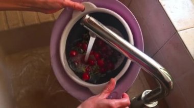 Yüksek açıdan çekilen yakın çekim, kadının ellerinin mutfakta kiraz yıkadığını gösteriyor..