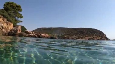Denizin içinden çekilen çekim, insanların plajda yüzdüğü sakin suyu gösteriyor. Arka planda güzel mavi gökyüzü.