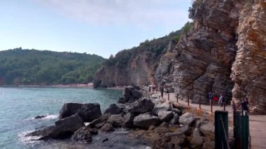 Budva, Karadağ - Eylül 04, 2024. Karadağ 'ın Budva kentindeki ünlü Mogren plajına giden ahşap bir platformda yürüyen insanlar. Tatil kavramı.