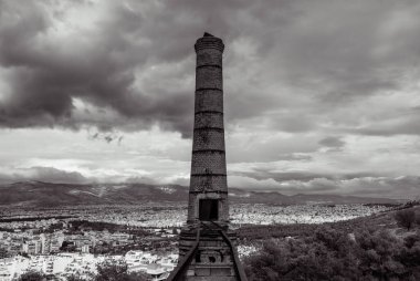 Black and white image of an old abandoned limekiln at the city of Athens in Greece. Dramatic clouds at the sky over the city. Travel concept. clipart