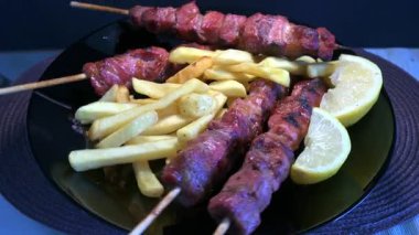 Yunan souvlaki domuz şişi, kızarmış patates ve limon dilimlerinin görüntüsü bir tabağın içinde dönüyor. Yiyecek konsepti.