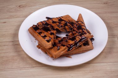 Tahta arka planda beyaz tabakta çikolatalı waffle.
