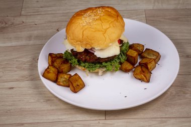 Tahta arka planda beyaz tabakta kızarmış patates ve tavuk burger.