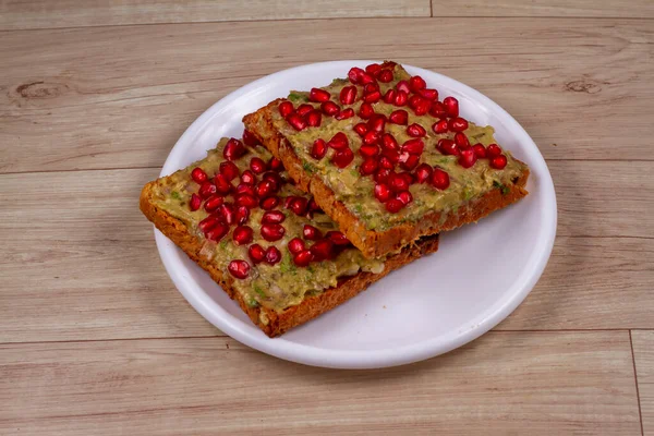 Avokado Toasties tahtadan arka planda beyaz tabakta nar tohumları