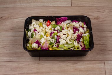 Ahşap zemin üzerinde siyah kapta Yunan Salatası