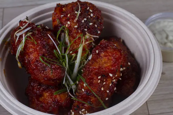 Sticky honey-soy chicken wings in bowl over wooden background.