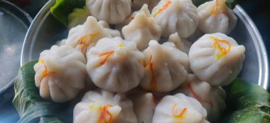 Maharashtrian sweet of Modak that is offered to Lord Ganesh, garnished with kesar (saffron) to be had with Ghee bowl and Lord Ganpati in the background. clipart