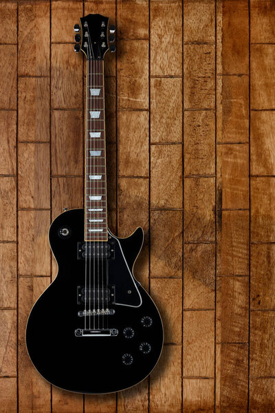 Black electric guitar on a distressed wooden backdrop with space for copy and a drop shadow